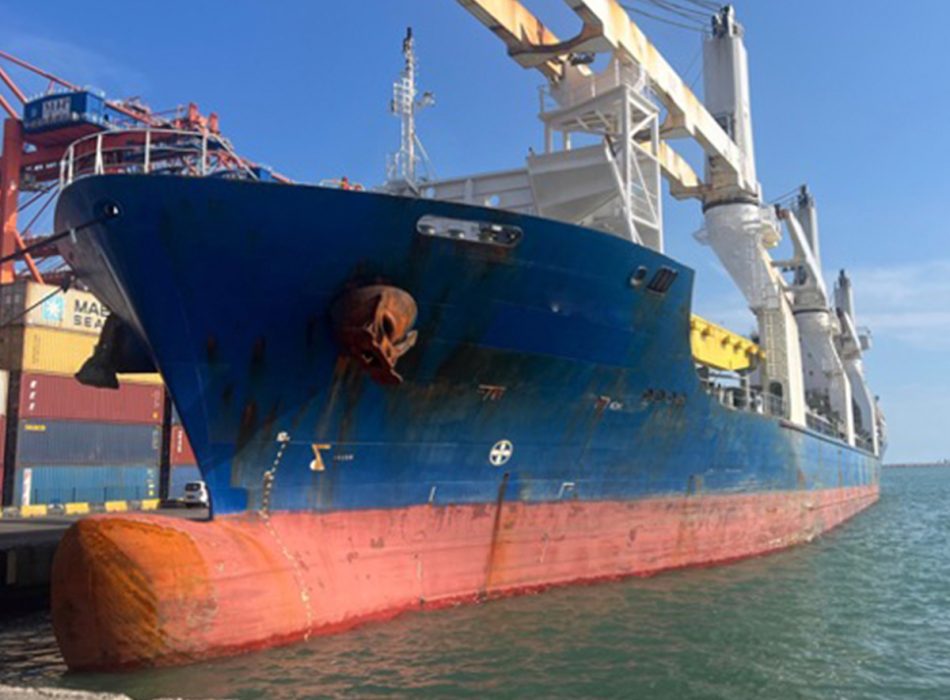 Cargo ship docked at port for asbestos inspection and removal under a clear blue sky.