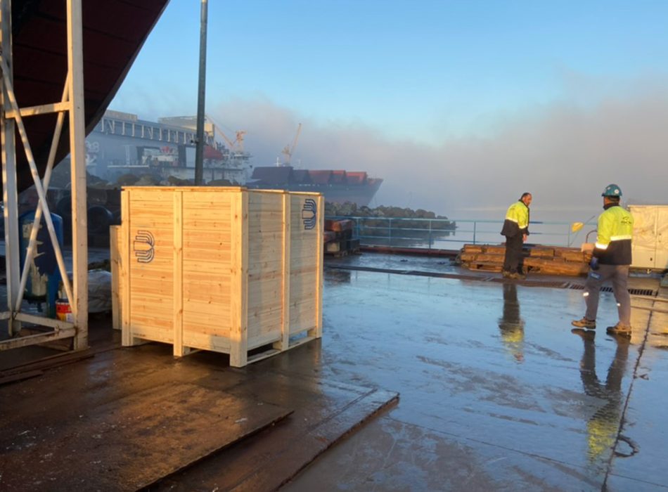 Maritime workers overseeing the delivery of wooden crates packed with spare parts on a wet dock.