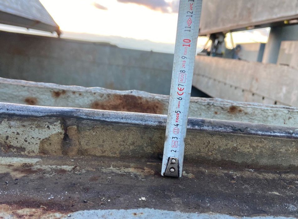 Technician measuring hatch cover wear in Turkey at sunset to ensure precise maintenance.